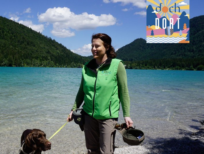 Rangerin Sabine Gerg mit ihrem Hund am Walchensee  - mit dem Podcastlogo von dochdort, Lisa Steinbacher, © Tölzer Land Tourismus|KUNZ PR